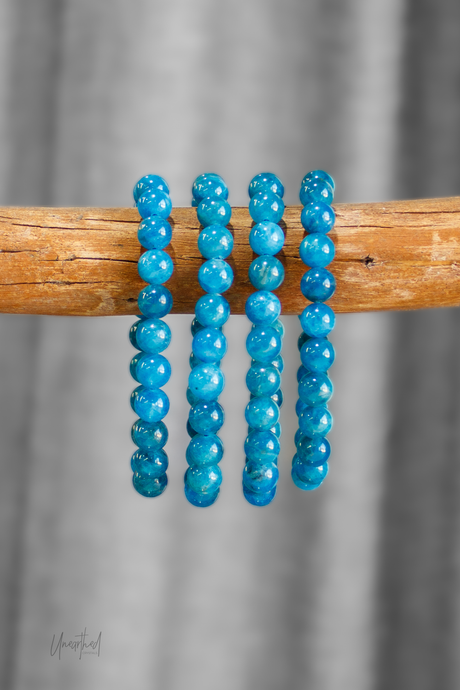 Four blue beaded bracelets on a wooden stick against a gray background