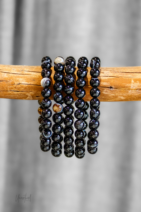 Black beaded bracelets on a wooden stick against a gray background