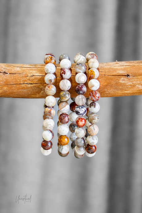 Three beaded bracelets on a wooden stick with a gray background
