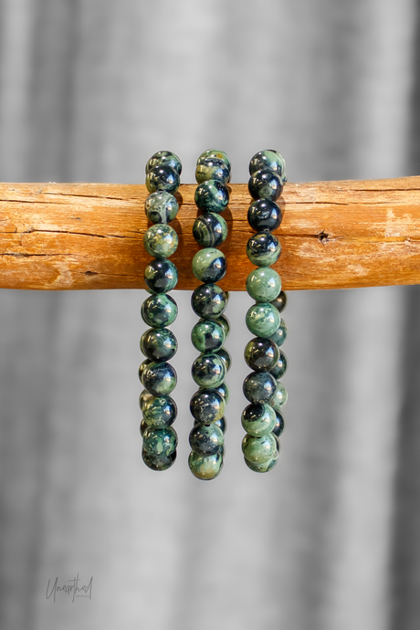 Green beaded bracelets on a wooden stick with a gray background