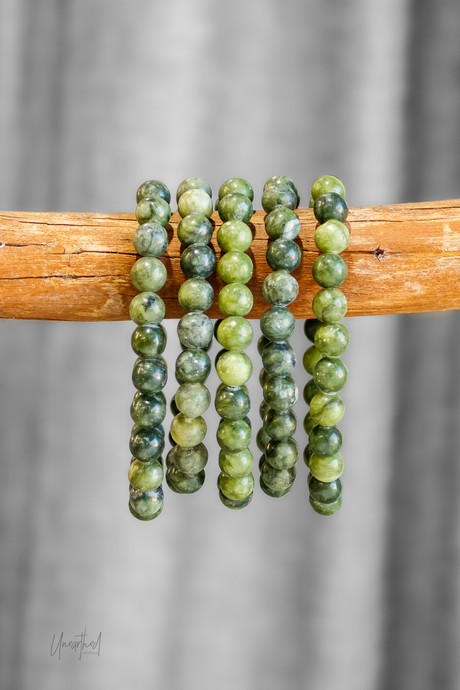 Green beaded bracelets on a wooden stick against a gray background