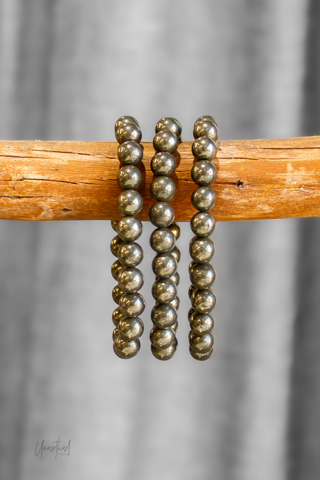 Pyrite beaded bracelets on a wooden stick with a gray curtain background