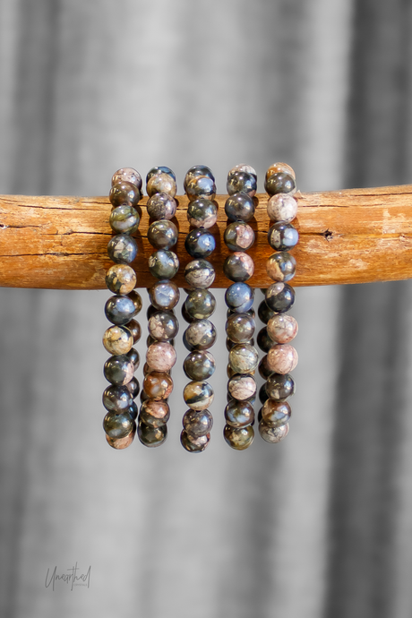 Set of beaded bracelets on a wooden stick against a gray background