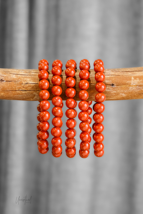 Red Jasper beaded bracelets on a wooden stick against a gray background