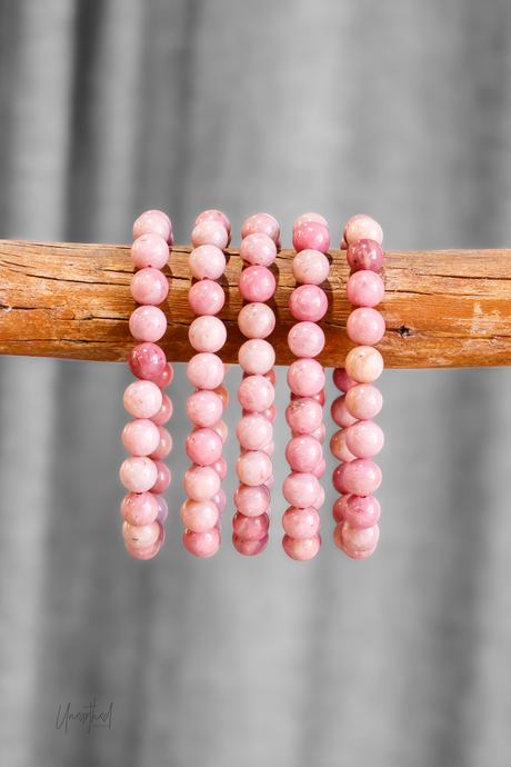 Set of pink beaded bracelets on a wooden stick with a gray background