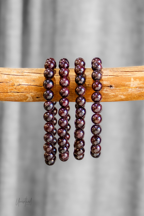 Three dark red beaded bracelets on a wooden stick against a gray background