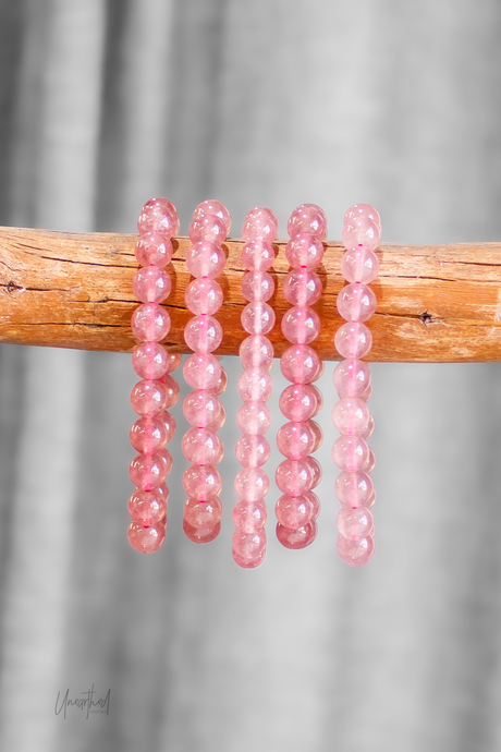 Pink beaded bracelets on a wooden stick against a gray background