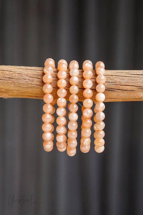 Set of peach-colored beaded bracelets on a wooden stick against a dark background
