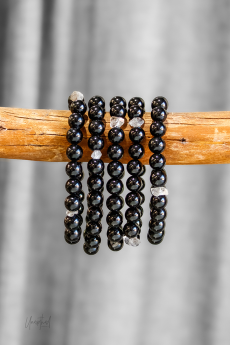Black beaded bracelets with quartz accents on a wooden stick against a gray background
