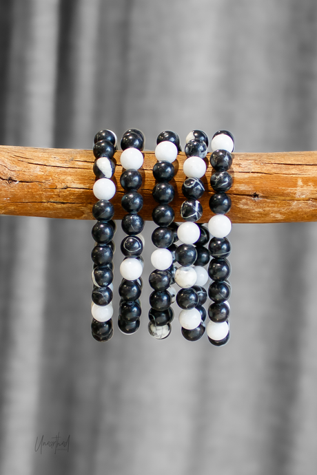 Black, white, and gray beaded bracelets on a wooden stick with a gray background