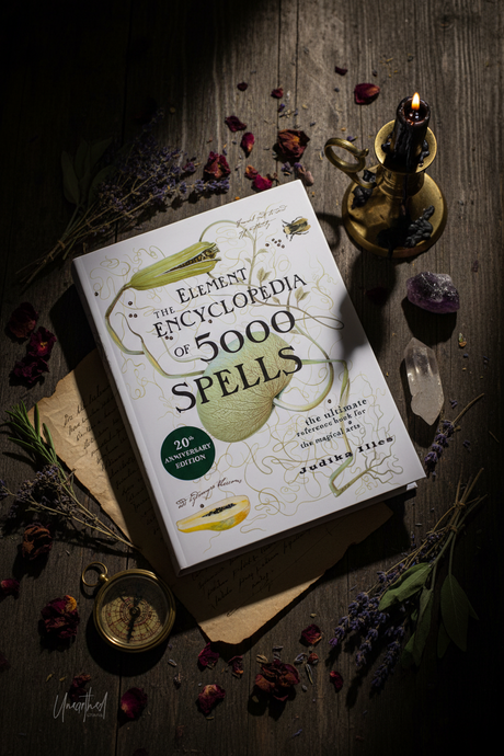 Book titled 'Encyclopedia of 5000 Spells' on a wooden surface with candles and herbs.