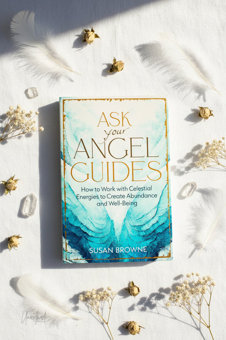 Book titled 'Ask Your Angel Guides' by Susan Browne on a white surface with feathers and flowers.