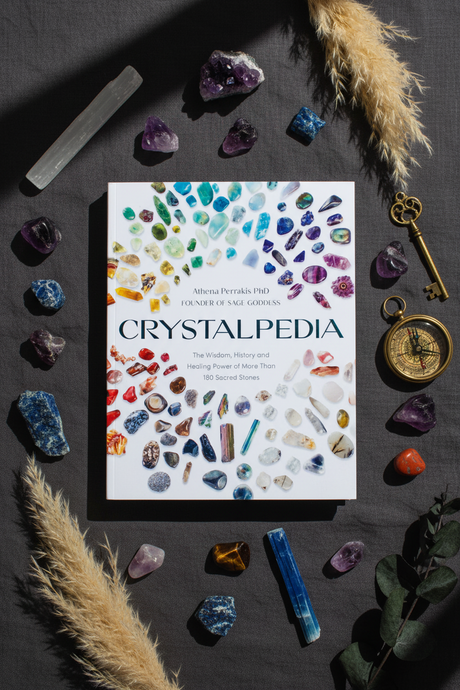 Book titled 'Crystalpedia' surrounded by crystals and decorative items on a dark surface
