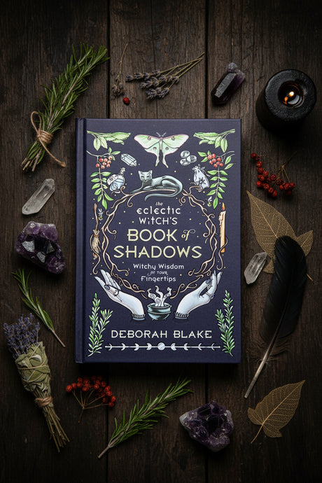 The book cover of 'The Eclectic Witch's Book of Shadows' by Deborah Blake, featuring a deep navy blue background adorned with vintage-style illustrations of a moth, a snake, hands, and botanical elements in gold, green, and white.