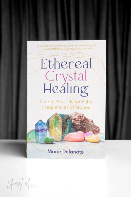 Book titled 'Ethereal Crystal Healing' by Marie Delanote on a white surface with a dark curtain background.