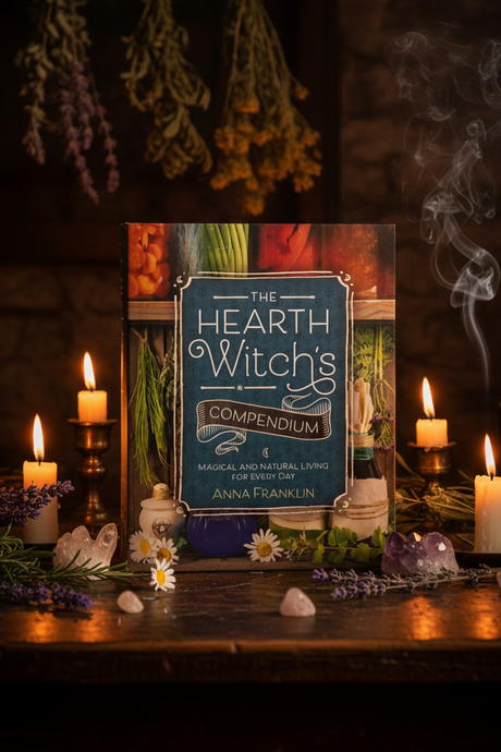 Hearth Witch's Compendium book on a table with candles and herbs in a dark setting