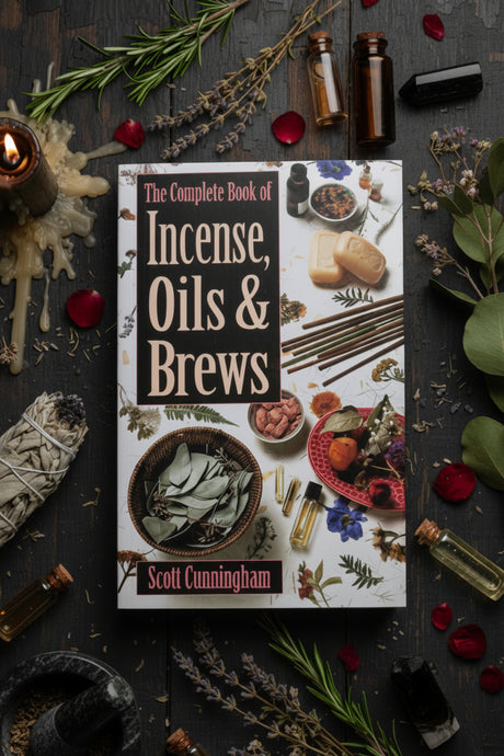Book titled 'The Complete Book of Incense, Oils & Brews' by Scott Cunningham surrounded by herbs and bottles on a dark surface.