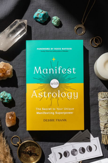 Book titled 'Manifest with Astrology' by Debbie Frank surrounded by crystals and a compass on a dark surface.