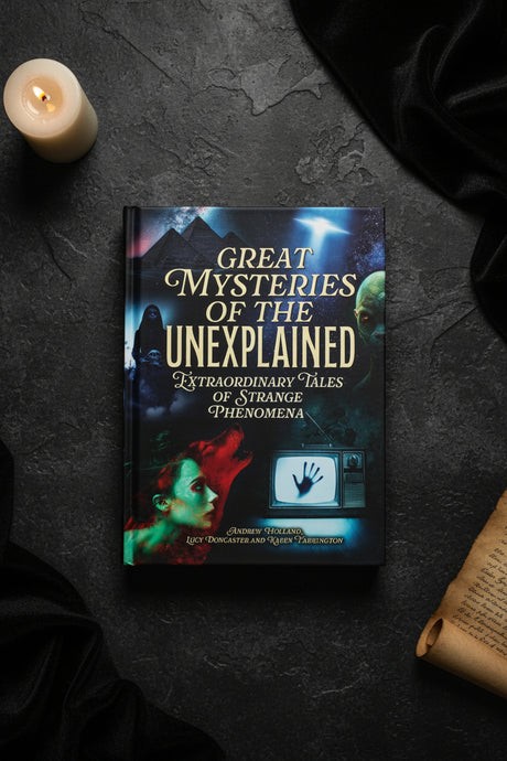 Book titled 'Great Mysteries of the Unexplained' on a dark surface with a candle and fabric.