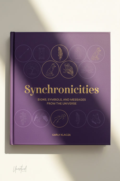 Purple book titled 'Synchronicities' with gold illustrations on a white background