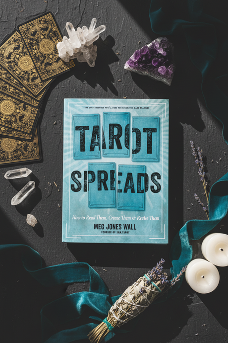 Book titled 'Tarot Spreads' with tarot cards, crystals, and candles on a dark surface