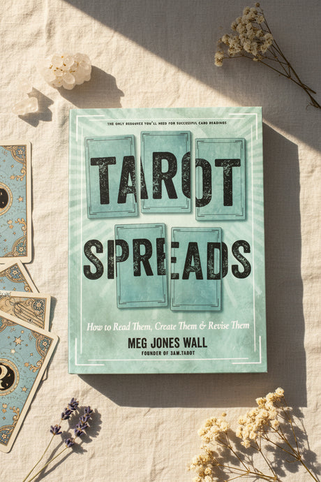 Book titled 'Tarot Spreads' by Meg Jones Wall on a textured surface with dried flowers.