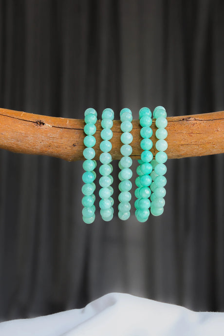 Amazonite beaded bracelets on a wooden stick against a dark background