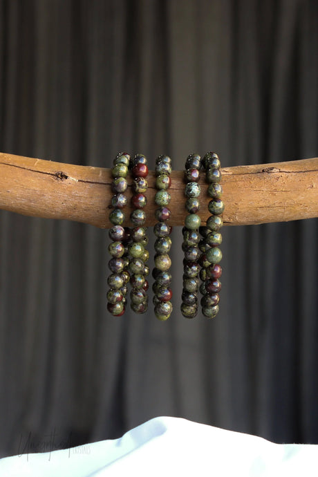 Three Dragons Blood Jasper beaded bracelets on a wooden stick against a dark background