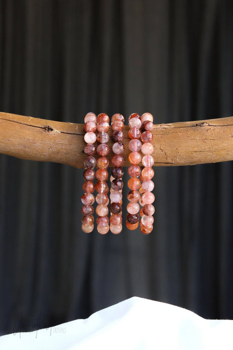 Set of Fire Quartz beaded bracelets on a wooden stick against a black background