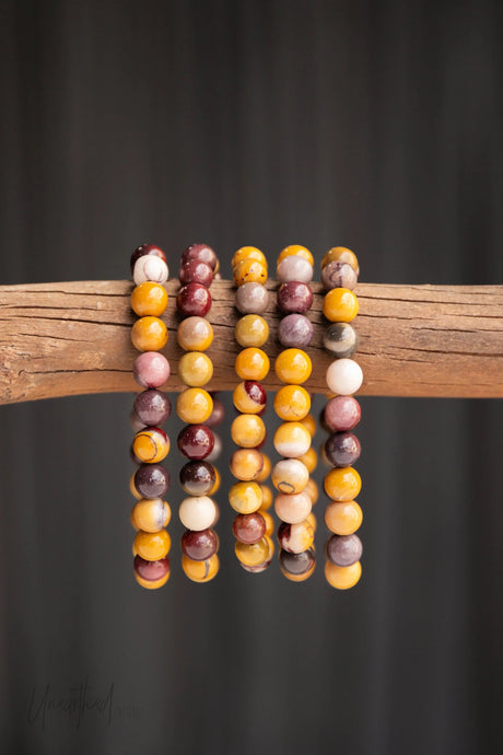 Multicolored Mookaite Jasper beaded bracelets on a wooden stick against a dark background