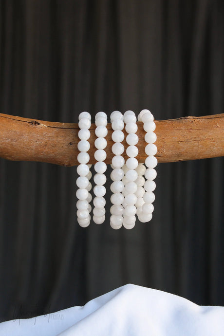 White Moonstone beaded bracelets on a wooden branch against a black background