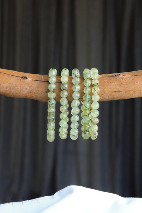 Green Prehnite beaded bracelet on a wooden stick against a dark background