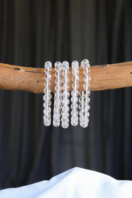 Set of clear quartz beaded bracelets on a wooden branch with a dark background