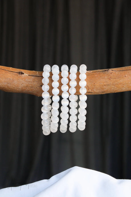 Set of Selenite beaded bracelets on a wooden branch against a black background
