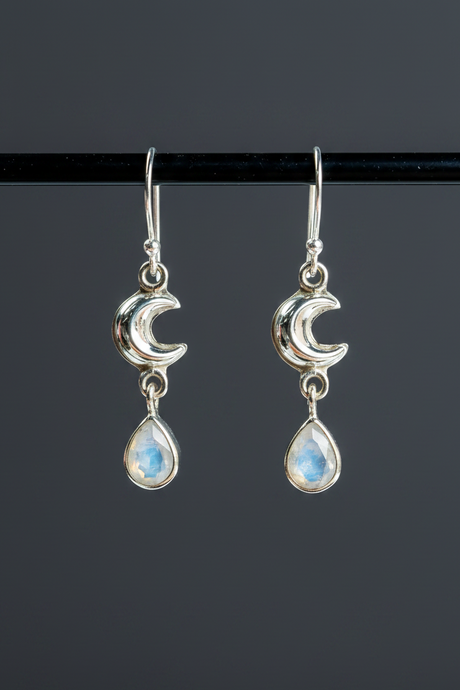 Silver earrings with moon designs and teardrop-shaped gemstones on a black background
