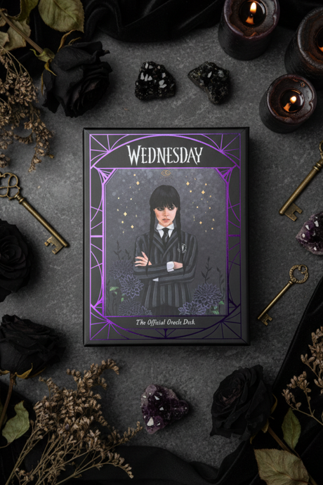Framed oracle cards titled 'Wednesday' with gothic design elements on a dark surface with candles and flowers.