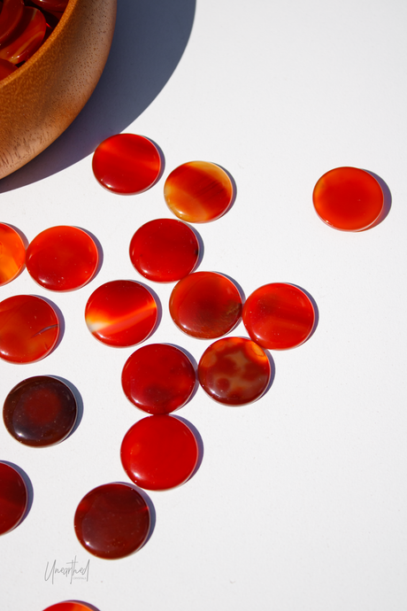Carnelian stones on a white surface with a wooden bowl.