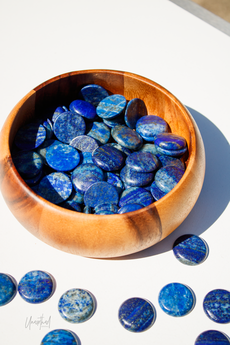 Wooden bowl filled with blue Lapis Lazuli stones on a white surface