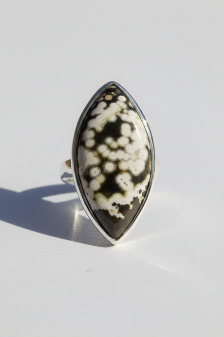 A silver ring featuring a large, marquise-shaped cabochon gemstone with a natural black and cream agate or jasper pattern, photographed on a clean white surface with a soft shadow.