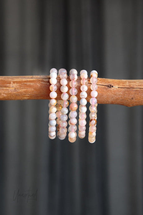 Five Flower Agate beaded bracelets on a wooden stick against a dark background