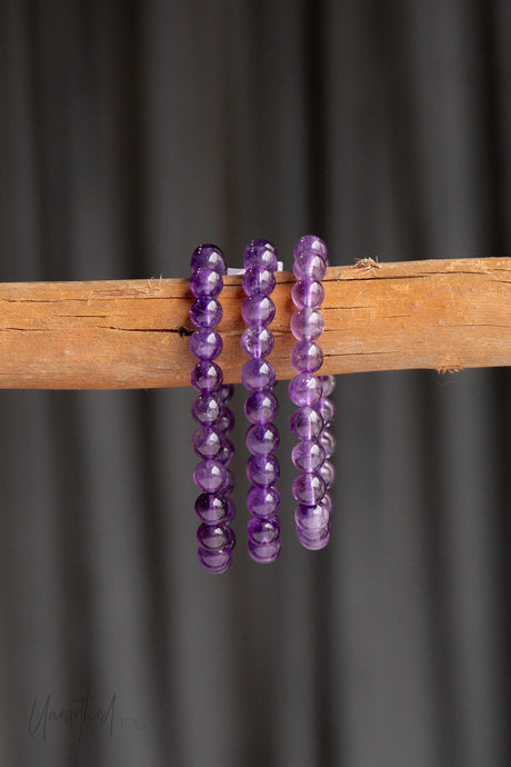Amethyst beaded bracelets on a wooden stick against a dark background