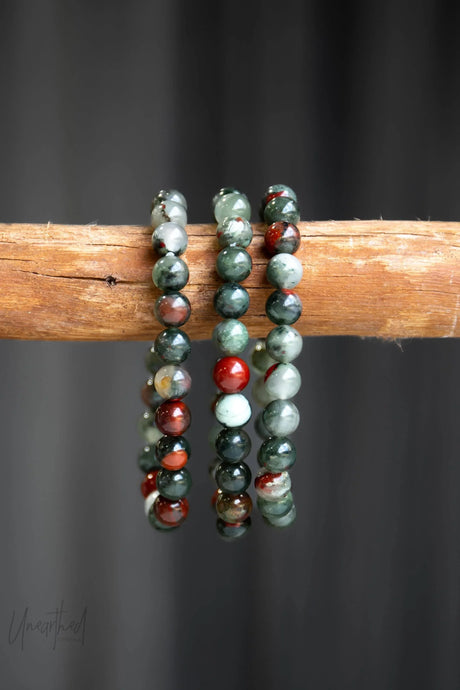 African Bloodstone Jasper beaded bracelets on a wooden stick against a dark background