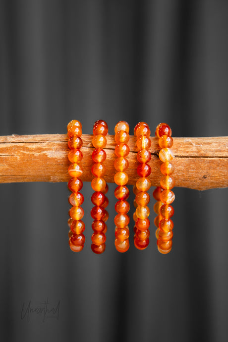 Carnelian beaded bracelets on a wooden stick against a dark background