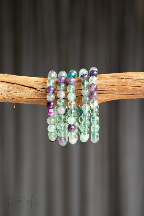 Set of Rainbow Fluorite beaded bracelets on a wooden branch with a dark background