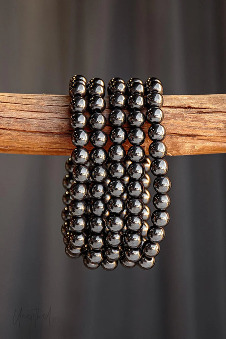 Hematite beaded bracelet on a wooden stick against a dark background