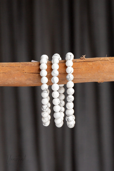 White Howlite beaded bracelets on a wooden stick against a dark background