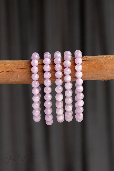 Set of Catseye pink Kunzite beaded bracelets on a wooden stick against a dark background