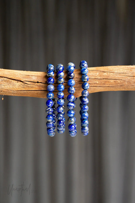 Blue Lapis Lazuli beaded bracelets on a wooden stick against a gray background