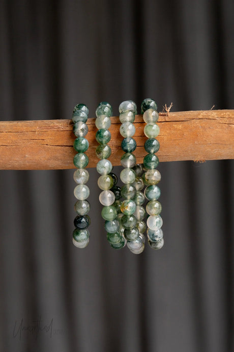 Moss Agate beaded bracelets on a wooden stick against a dark background