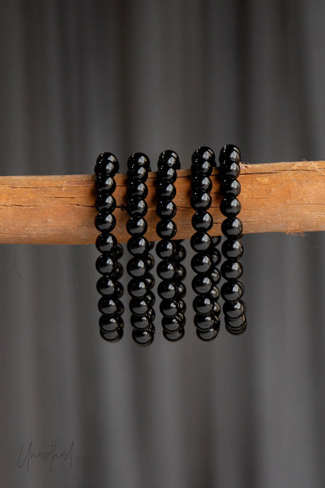 Black Obsidian beaded bracelet on a wooden stick against a gray background